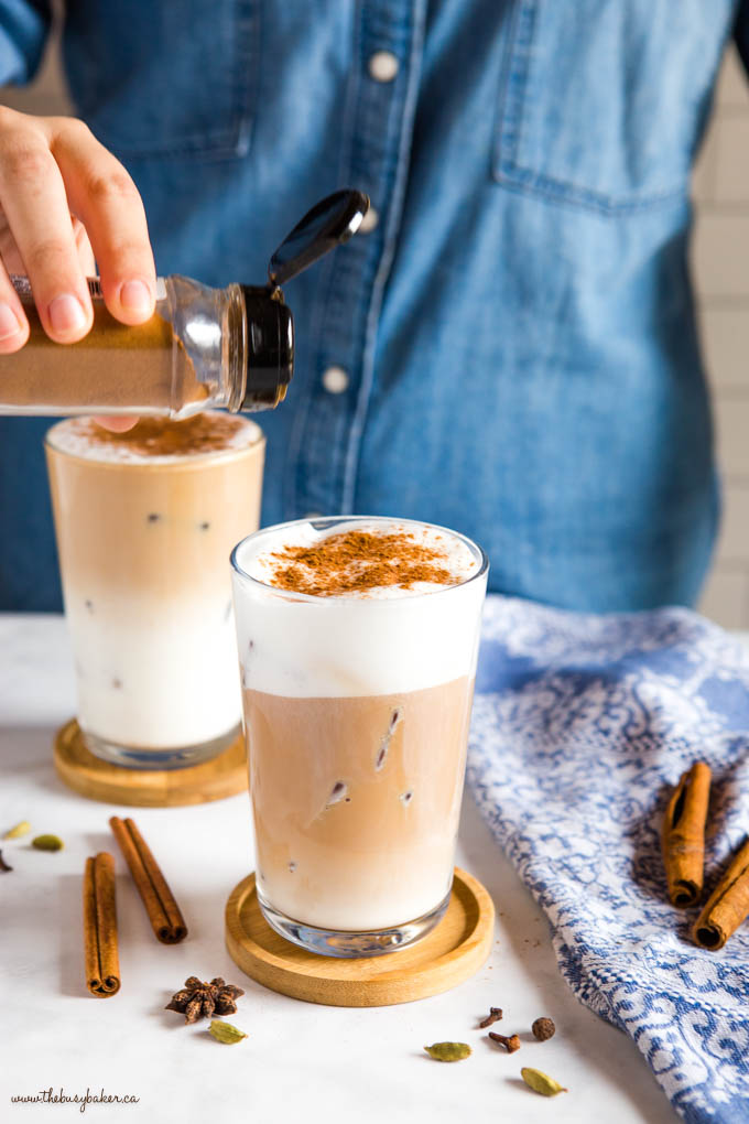 woman sprinkling cinnamon on top of chai latte with ice