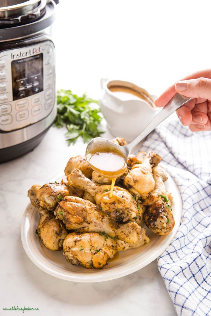 hand pouring gravy from a ladle onto chicken drumsticks