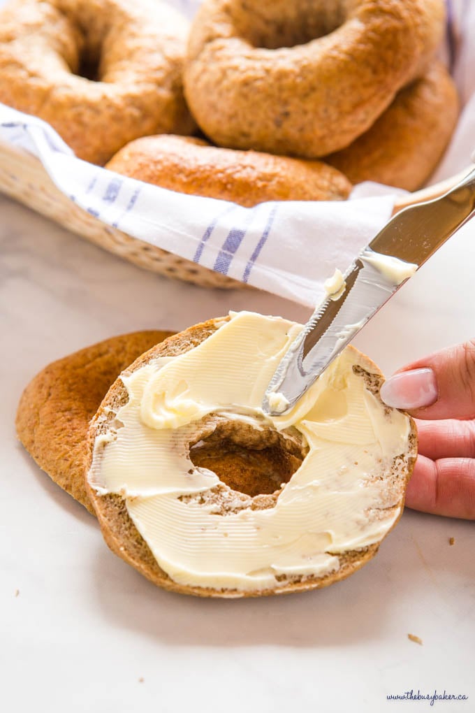 hand holding knife spreading butter on a whole wheat bagel