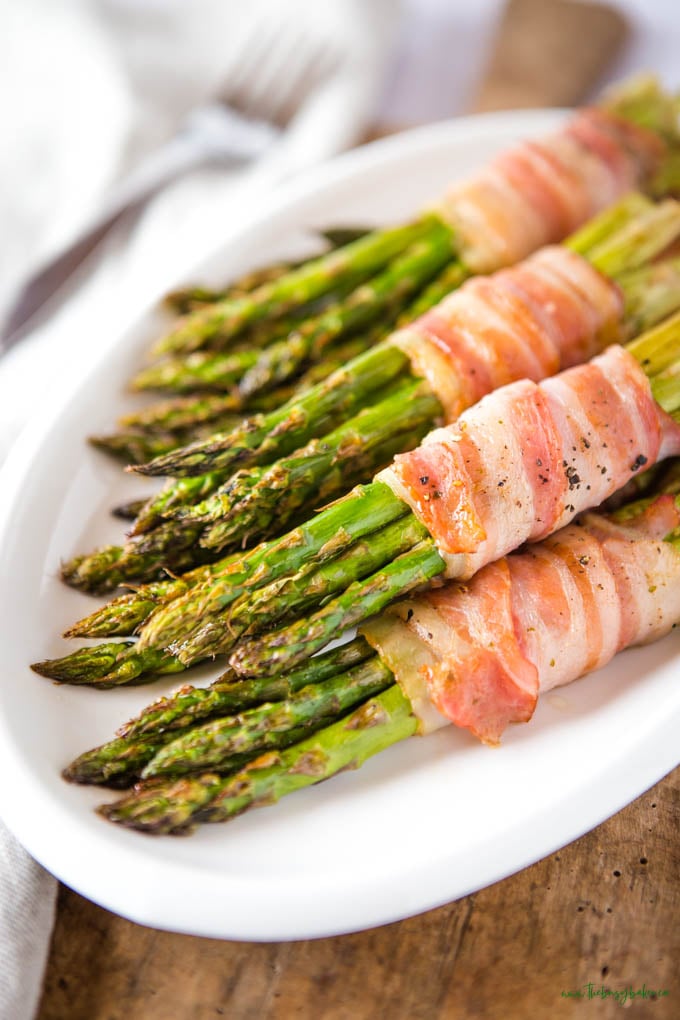 asparagus bundles wrapped in bacon on a white platter with black pepper