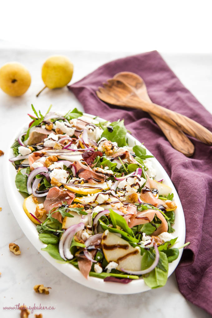 arugula salad on white planner with pears, prosciutto, goat cheese and walnuts
