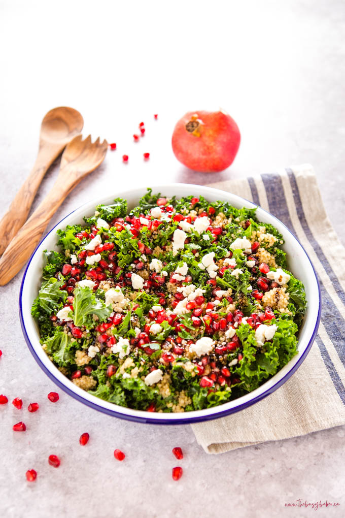 kale salad in white enamel bowl with pomegranate, goat cheese and quinoa