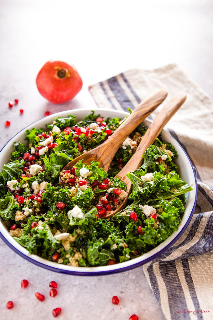 salad with kale, pomegranate, goat cheese and quinoa in an enamel bowl with wooden salad tongs