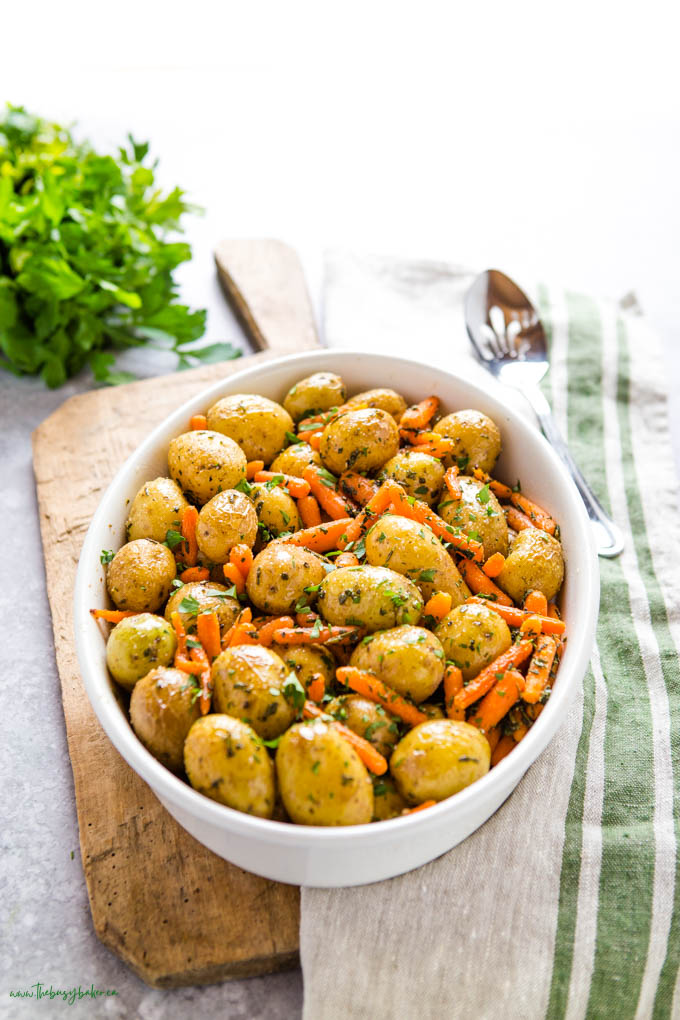 white oval baking dish with roasted potatoes and carrots and fresh herbs