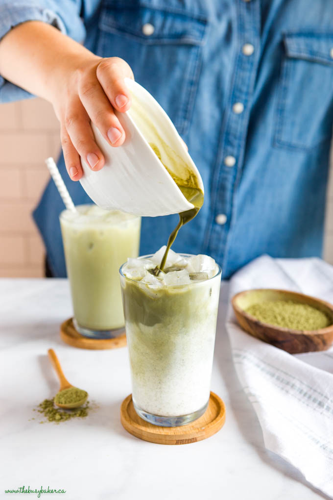 hand pouring matcha into glass with foamed milk and ice