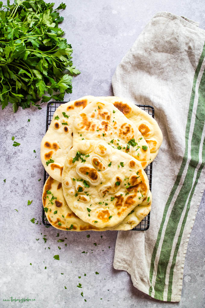 overhead image: naan bread on cooling rack with flour sack towel and green parsley