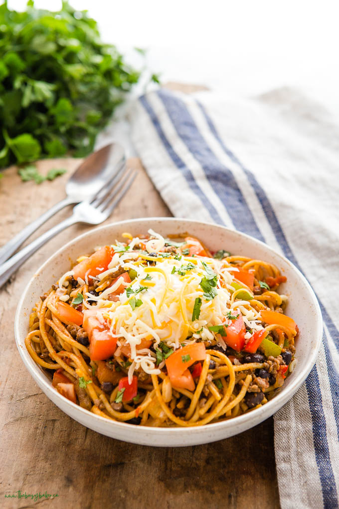 bowl of taco spaghetti with cheese and sour cream and tomatoes