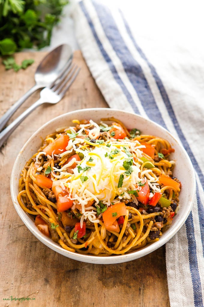 bowl of taco spaghetti with cheese, tomatoes, sour cream and cilantro