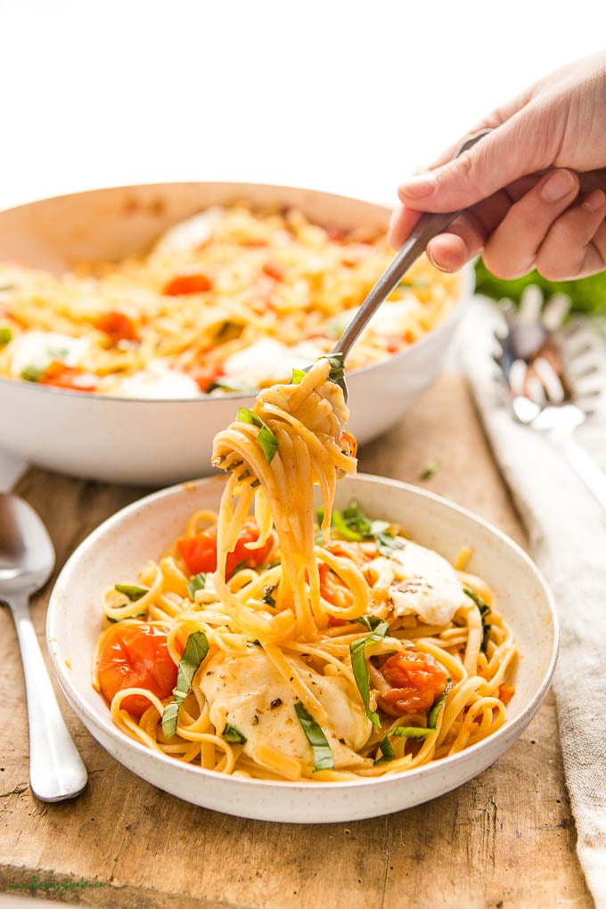 hand holding a forkful of pasta with basil, tomatoes and mozzarella