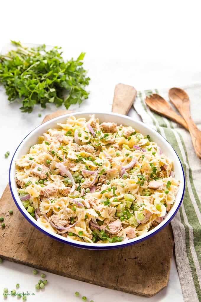 Tuna salad in white bowl on wood cutting board. a few peas scattered on counter