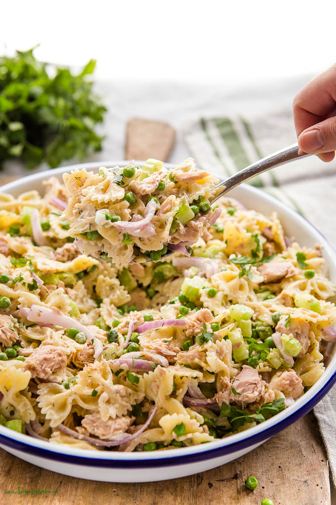 a hand holding a spoonful of the tuna salad- red onion, peas, butterfly pasta