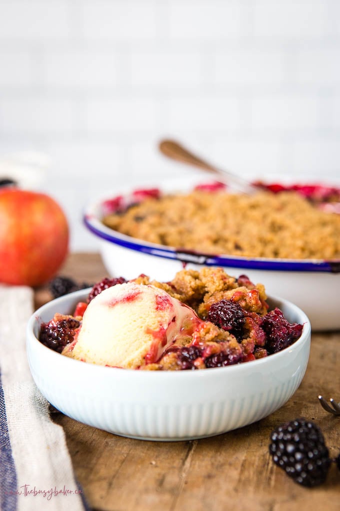 apple and blackberry crumble in blue bowl with a scoop of ice cream