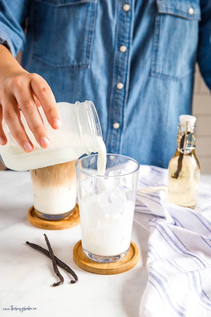 hand pouring foamed milk into glass with ice