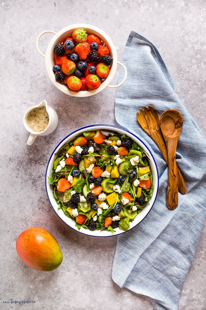 overhead image: salad in white enamel bowl with blue rim, with berries, mango and kiwi
