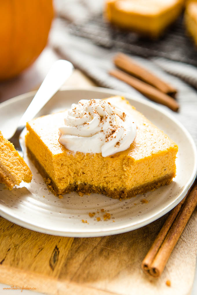closeup image: pumpkin cheesecake bar on plate with whipped cream