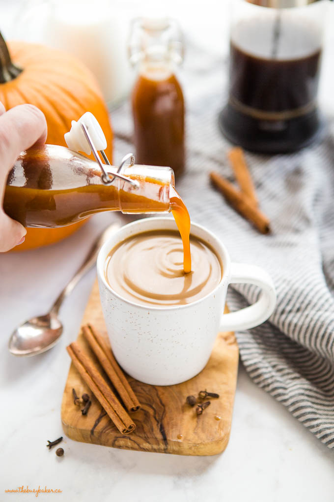 pouring homemade pumpkin spice syrup into coffee in a white mug