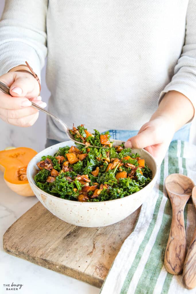 Spoonful of salad above large bowl of kale, butternut squash, nuts and bacon