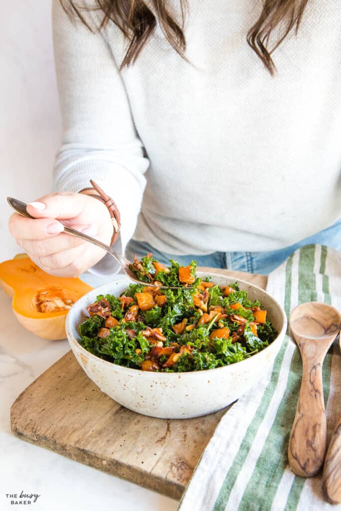 hand holding fork and scooping kale, butternut squash and nuts out of the bowl.
