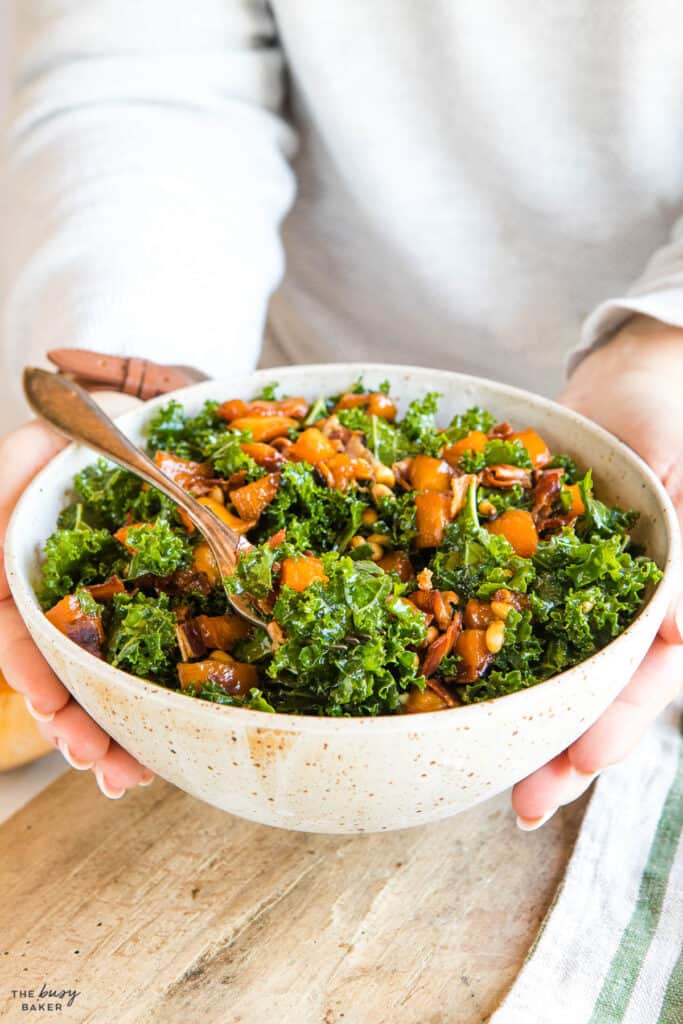 hands holding bowl of salad with fork resting in kale