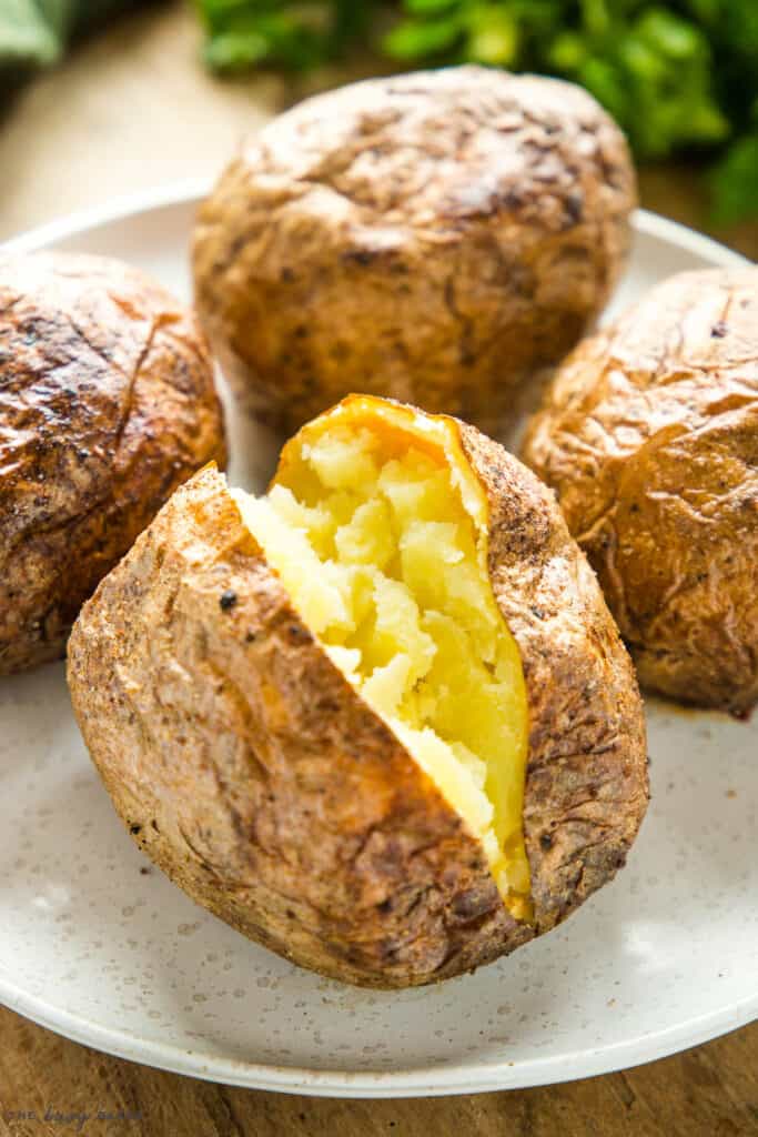 air fryer baked potato open on plate with fluffy inside and crispy skin