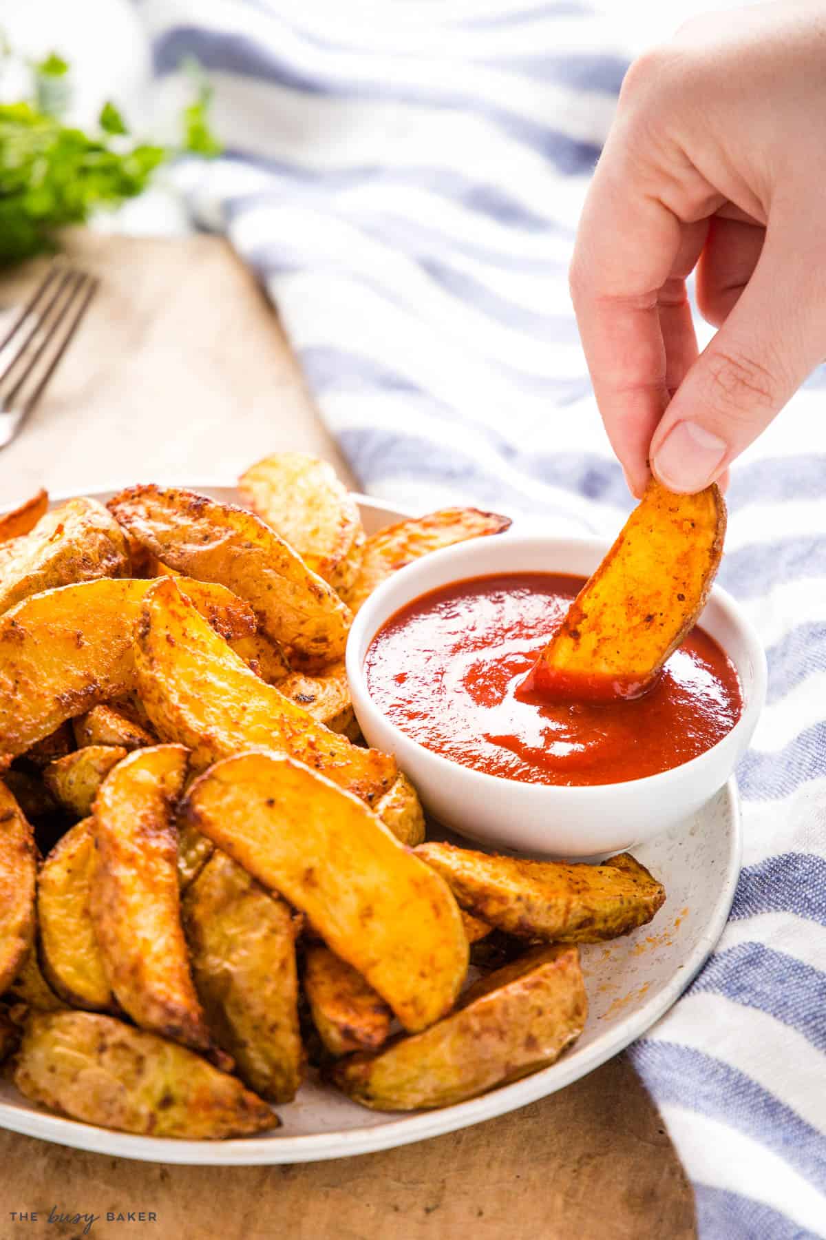 hand dipping crispy potato wedge in ketchup