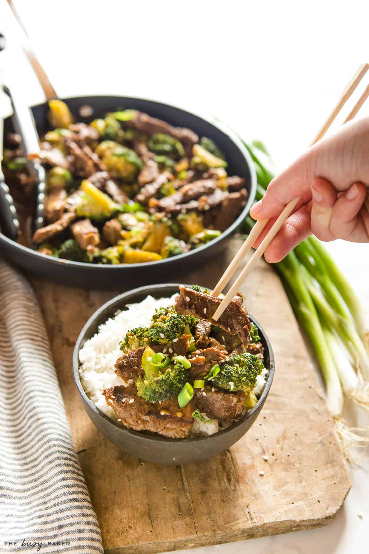 hand using chopsticks holding a piece of beef stir fry with broccoli