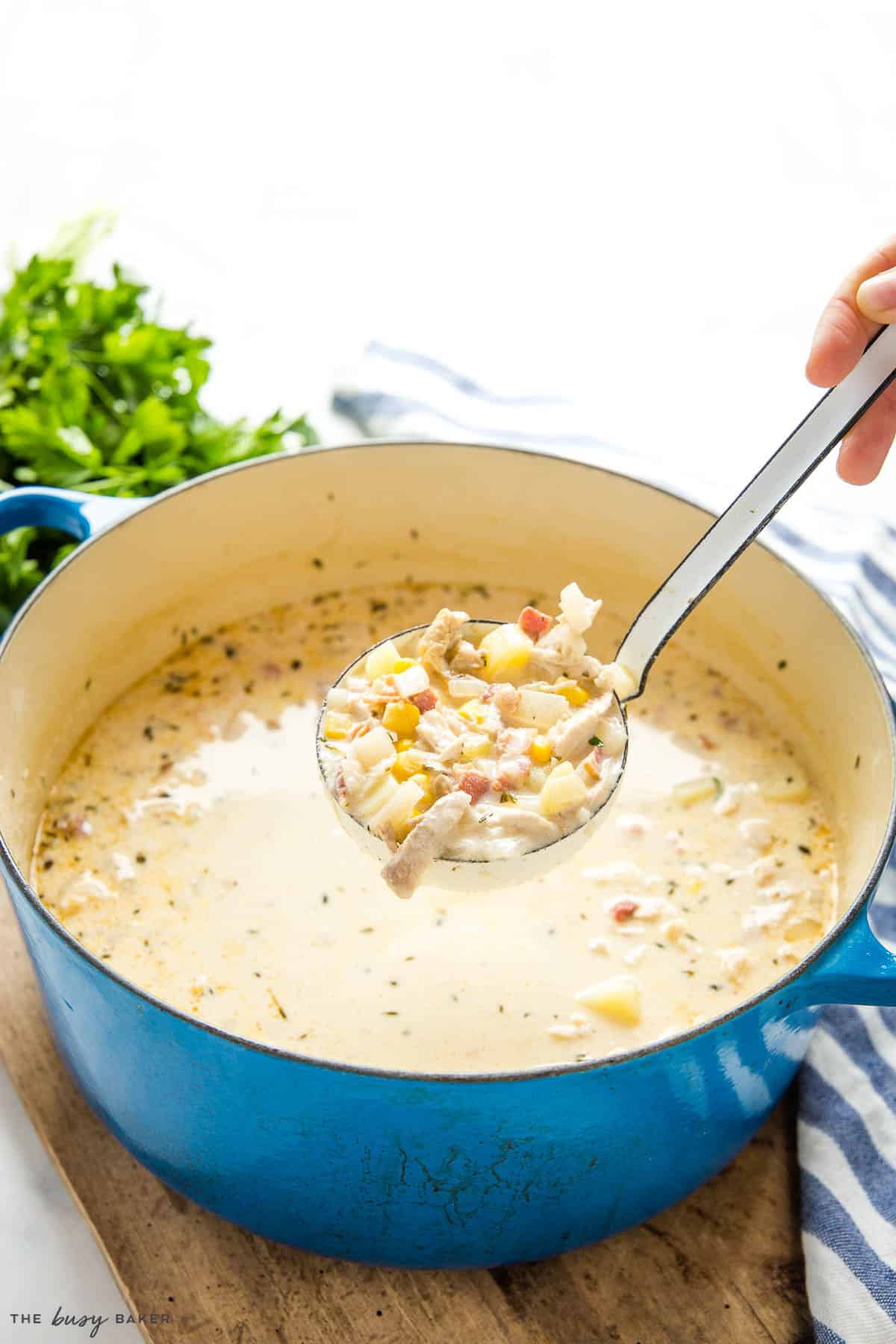 blue cast iron pot with a ladle of corn chowder with chicken