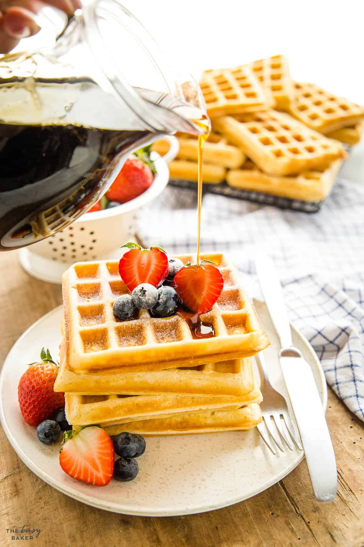 hand pouring maple syrup on a stack of waffles