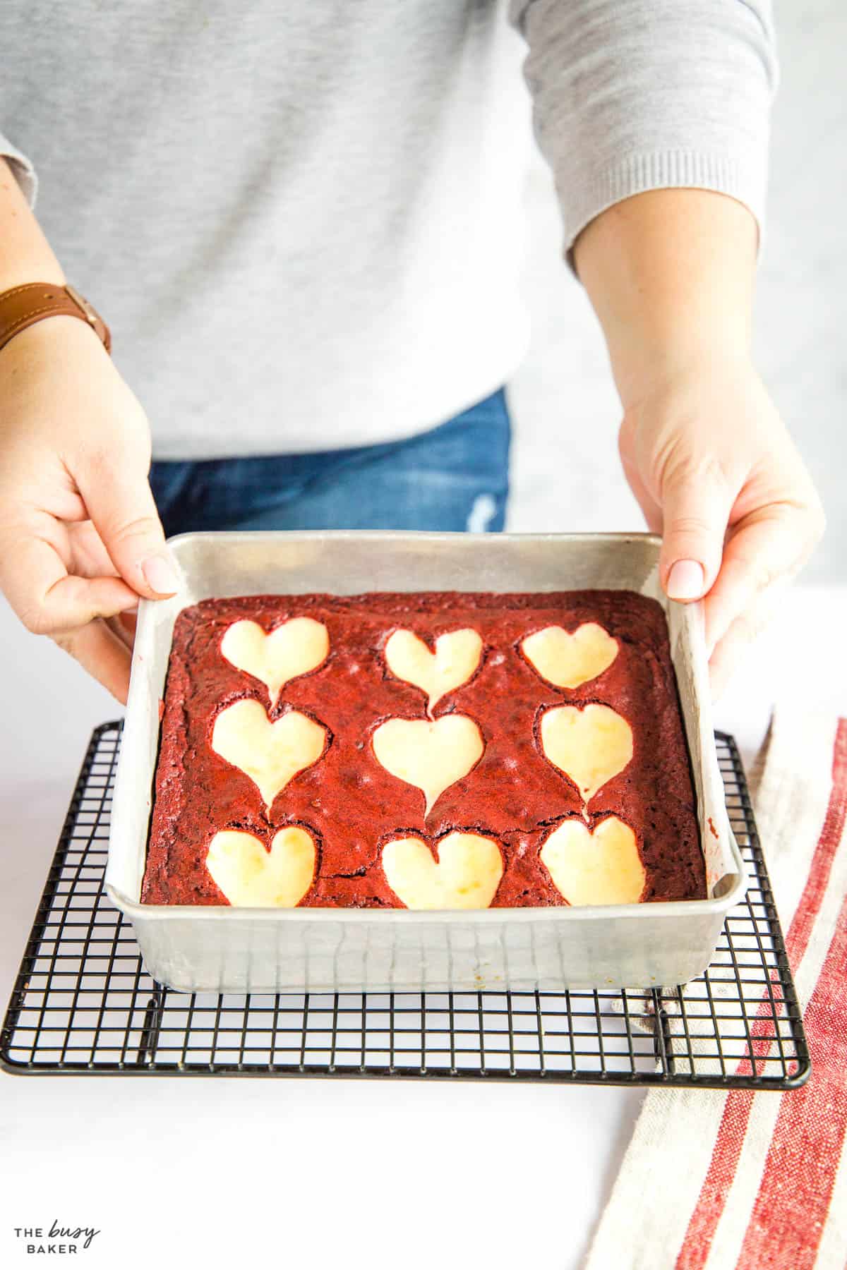 hand holding a pan of red velvet brownies with cheesecake hearts