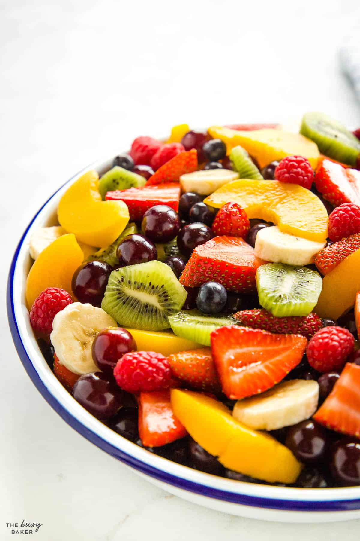 a bowl with banana slices, strawberries, raspberries, blueberries, kiwis, and peaches