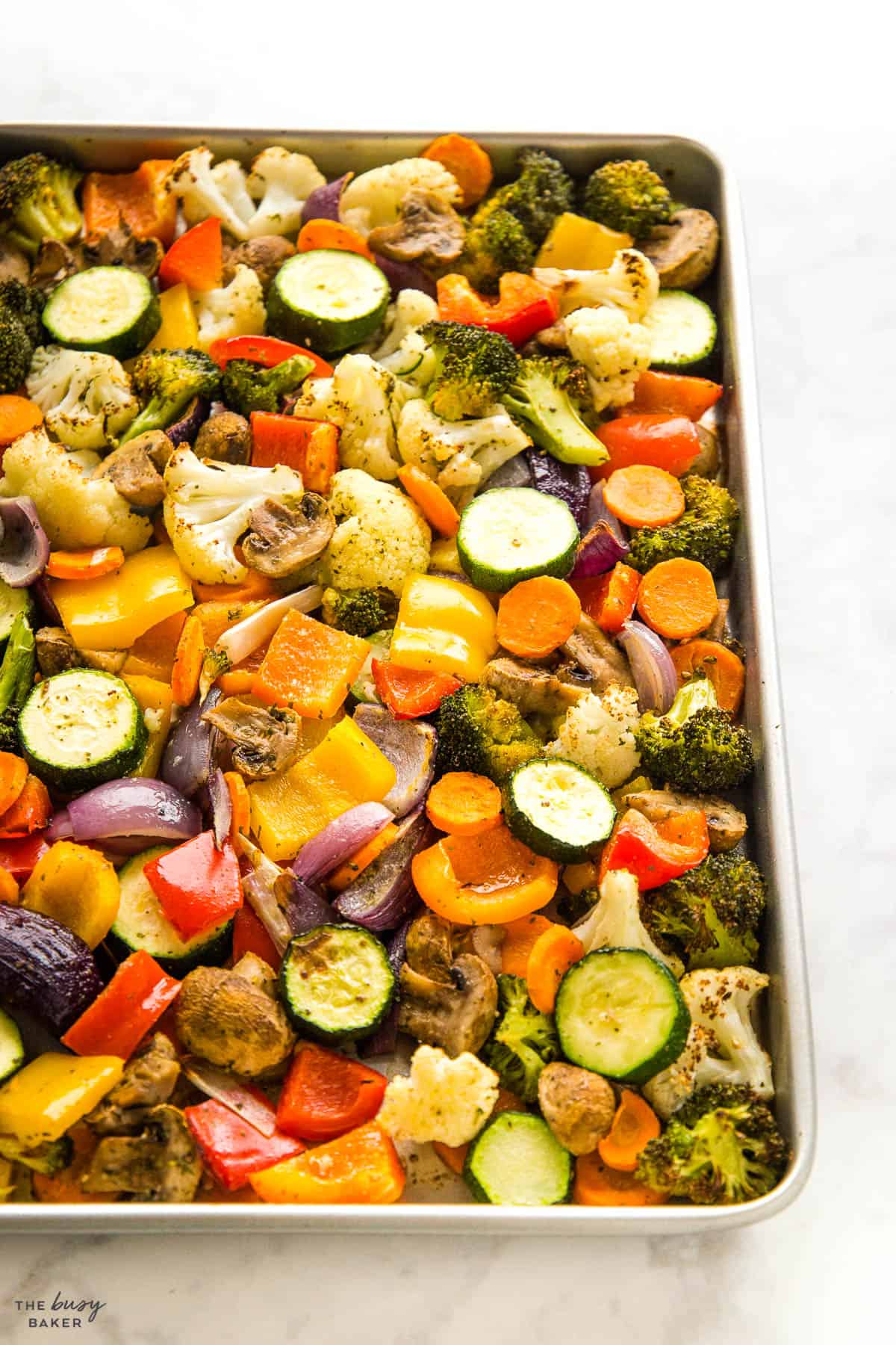 cauliflower, mushrooms, broccoli, peppers, carrots, onions, and zucchini on a sheet pan with seasoning