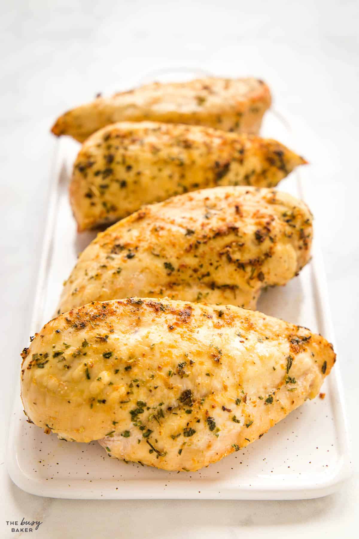 4 chicken breasts on a platter with herbs