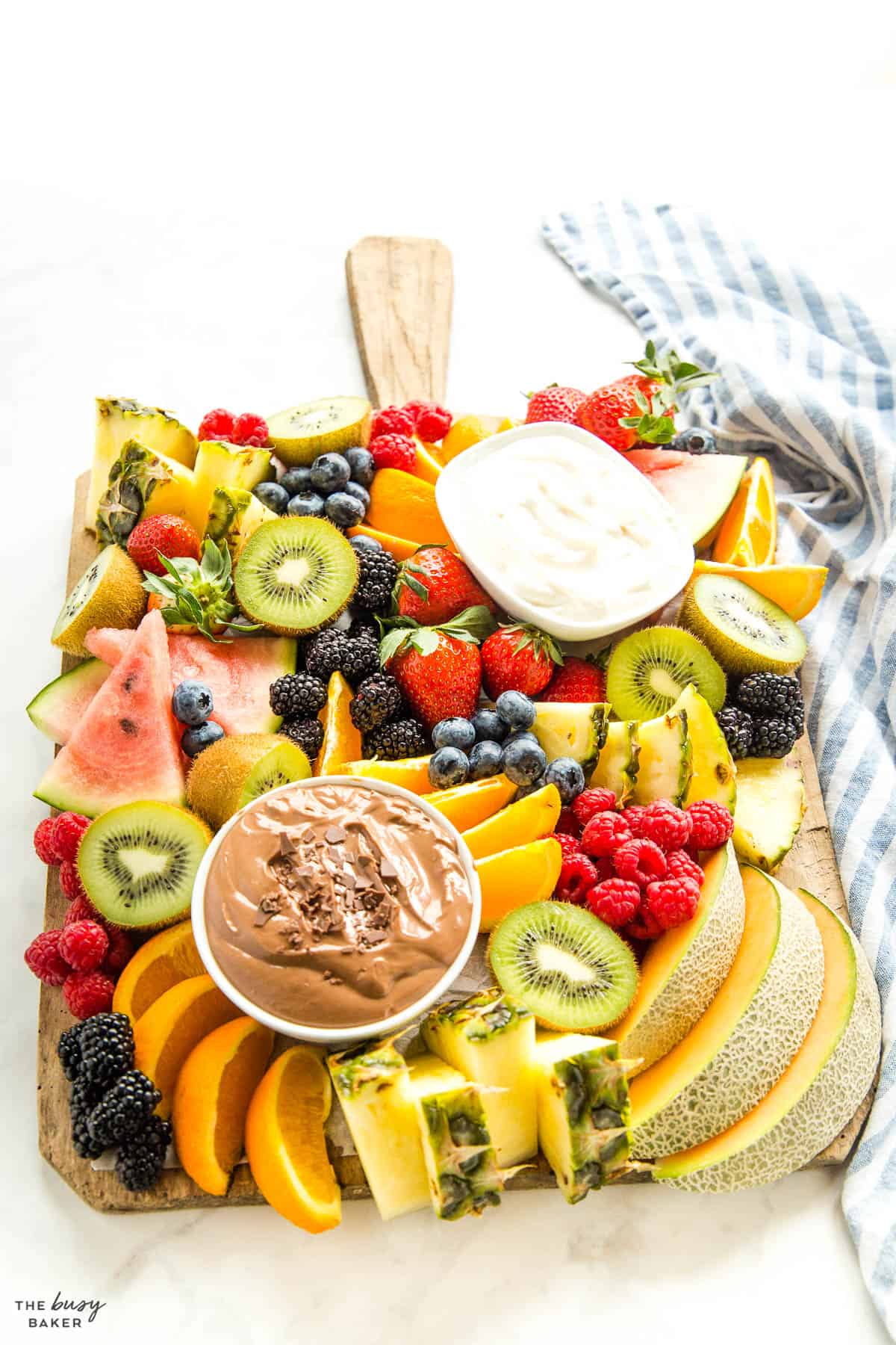 pineapple, kiwi, melons, and berries on a wooden board