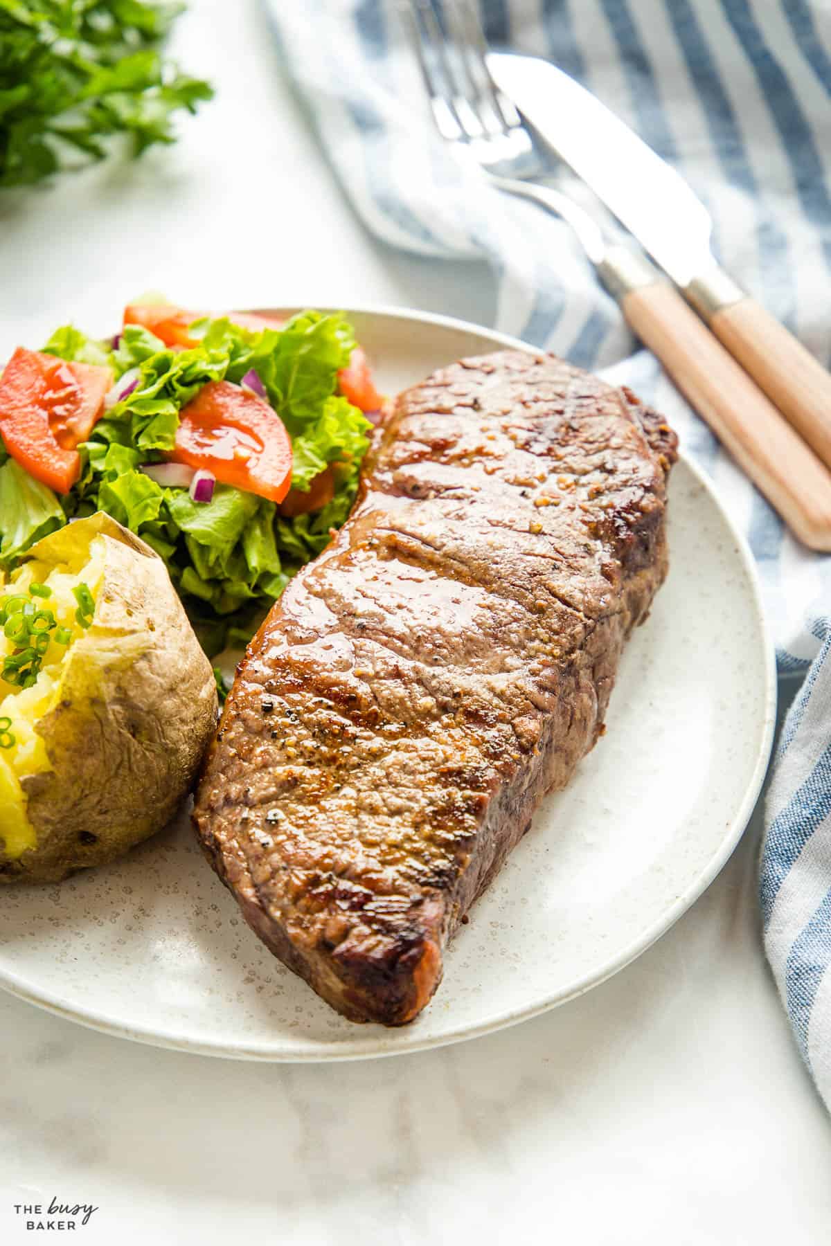 sirloin steak on plate with baked potato and salad
