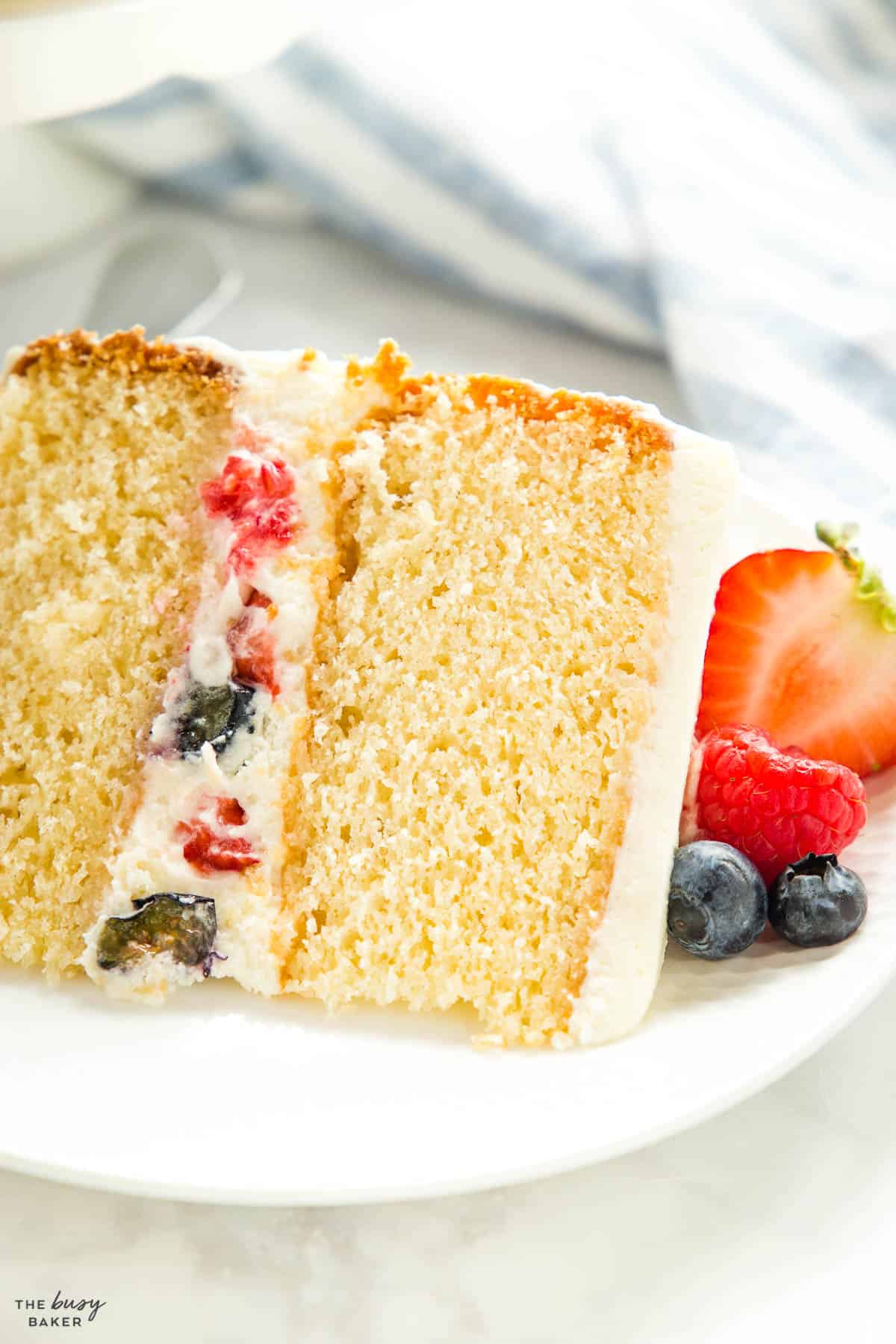 closeup image: slice of white cake with fresh berries and white cream frosting
