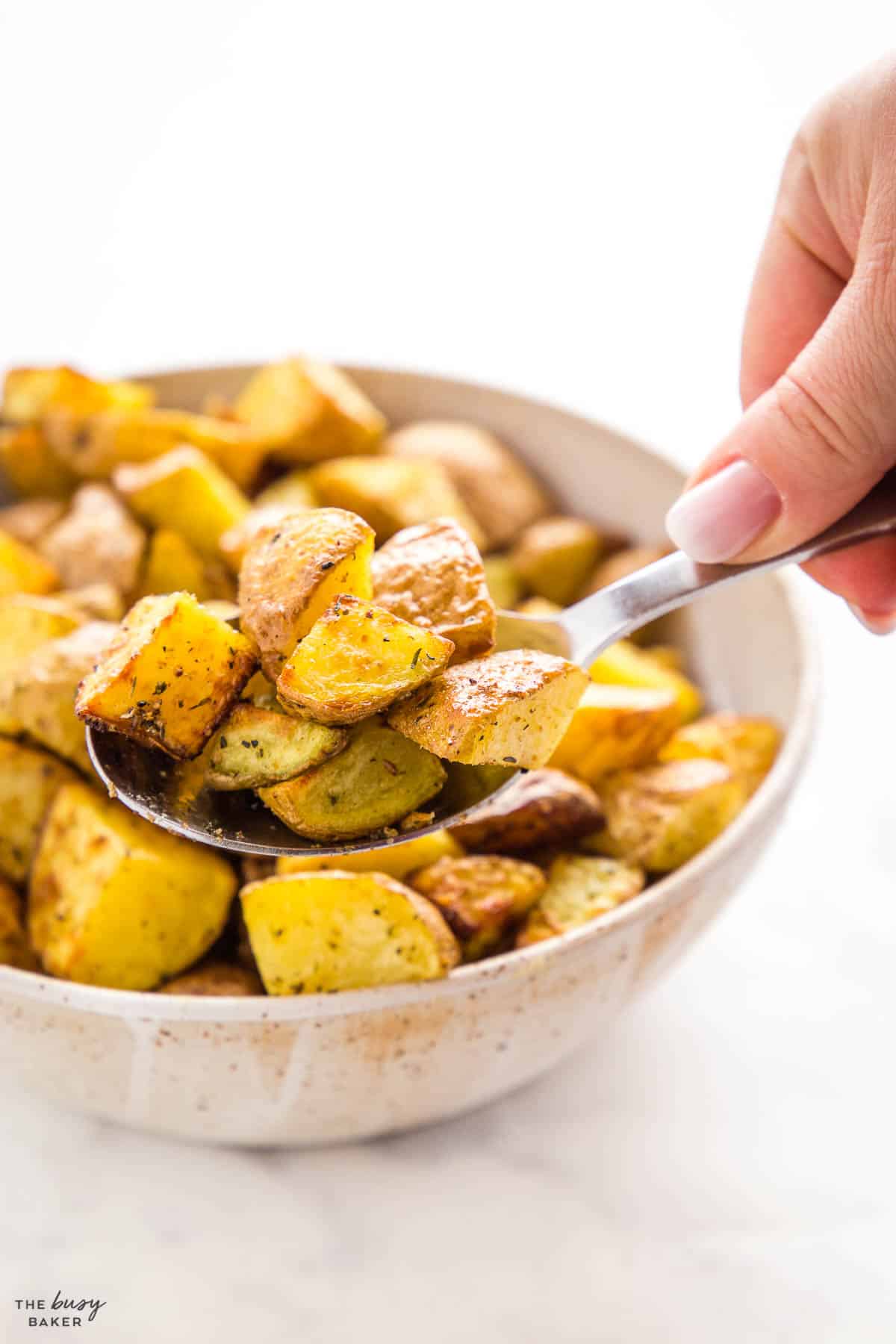 hand holding a spoon serving roasted potatoes