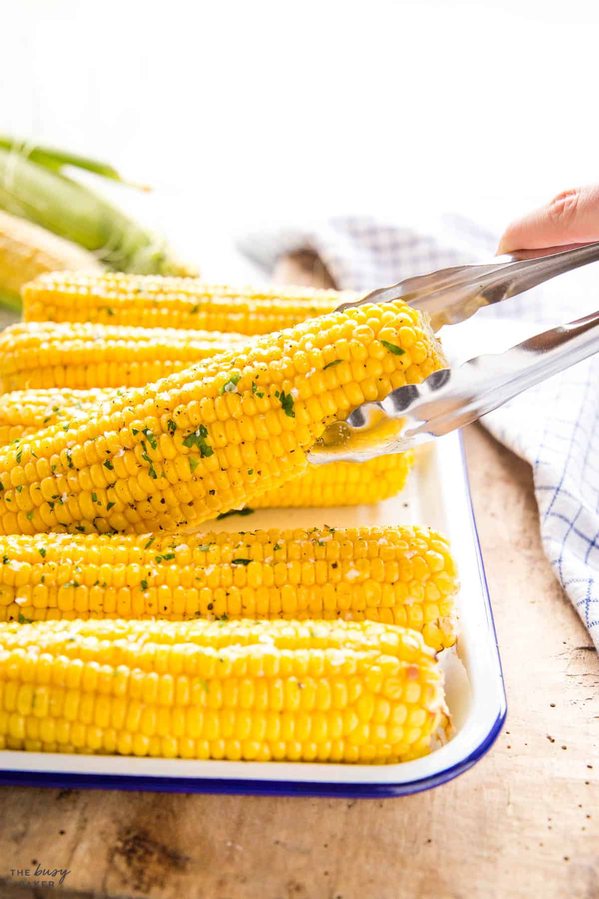 hand holding tongs serving an ear of corn