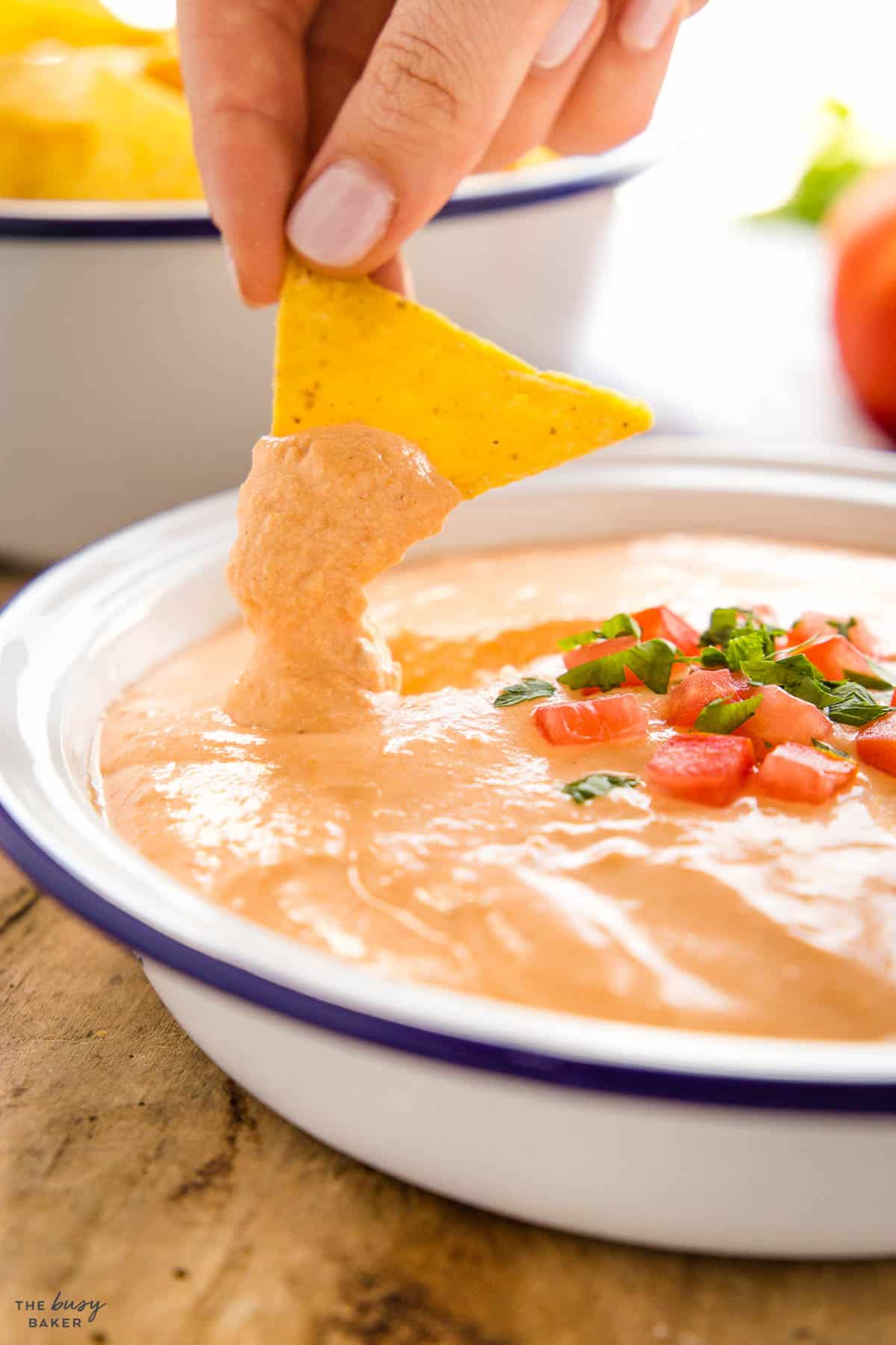 hand dipping a tortilla chip in cottage cheese queso dip