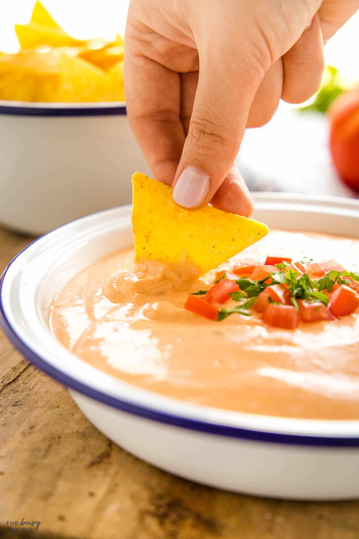 hand dipping tortilla chip in melted cheese appetizer
