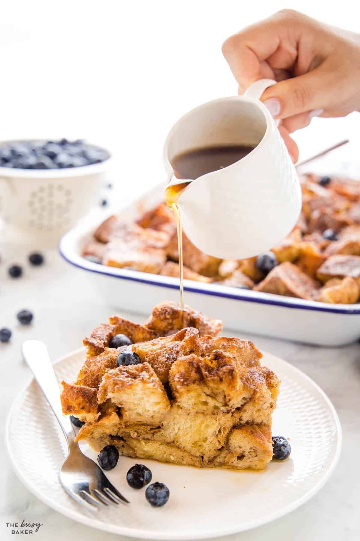 hand pouring syrup on a serving of french toast casserole with crispy cinnamon sugar topping