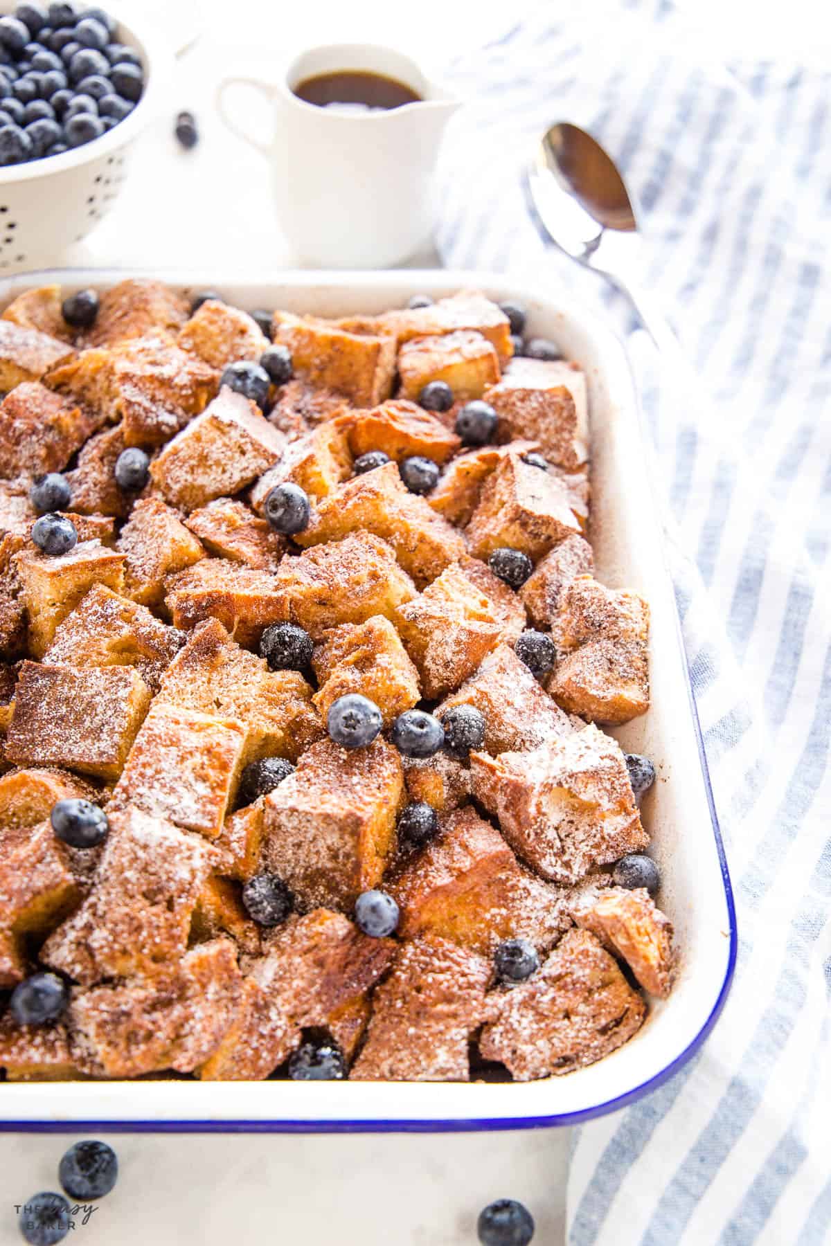 cinnamon sugar breakfast bake with blueberries and powdered sugar in a white baking pan