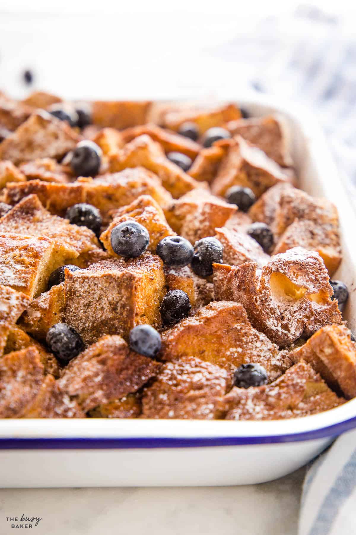 closeup image: overnight french toast casserole with powderd sugar and blueberries