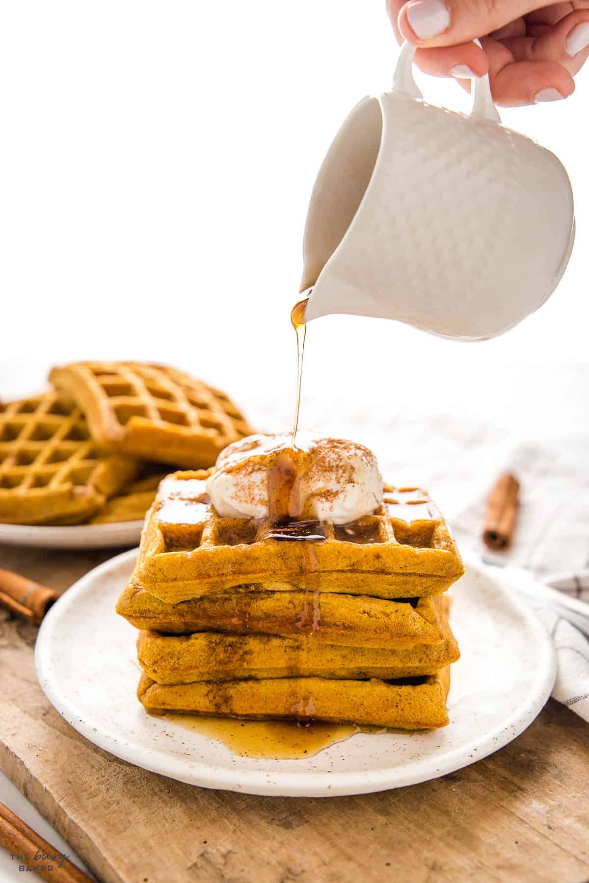 hand pouring syrup over stack of pumpkin waffles