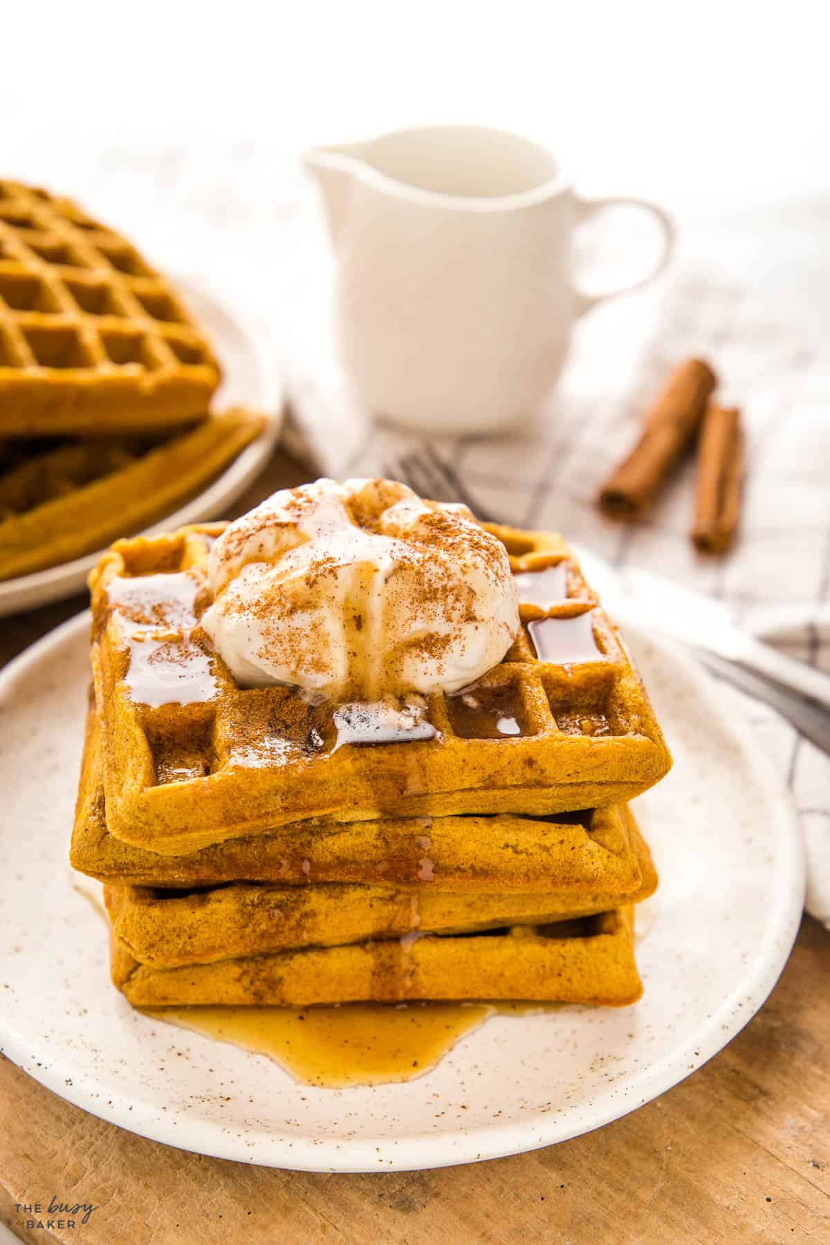 pumpkin waffles on a white plate with whipped cream and maple syrup