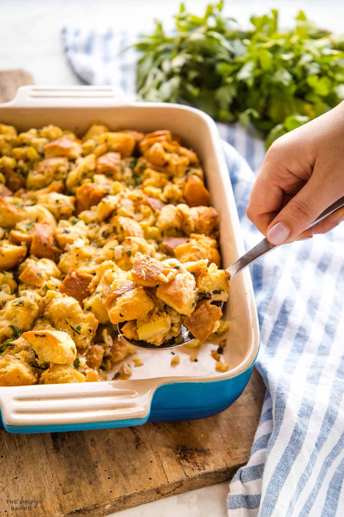 hand serving homemade stuffing from a baking dish