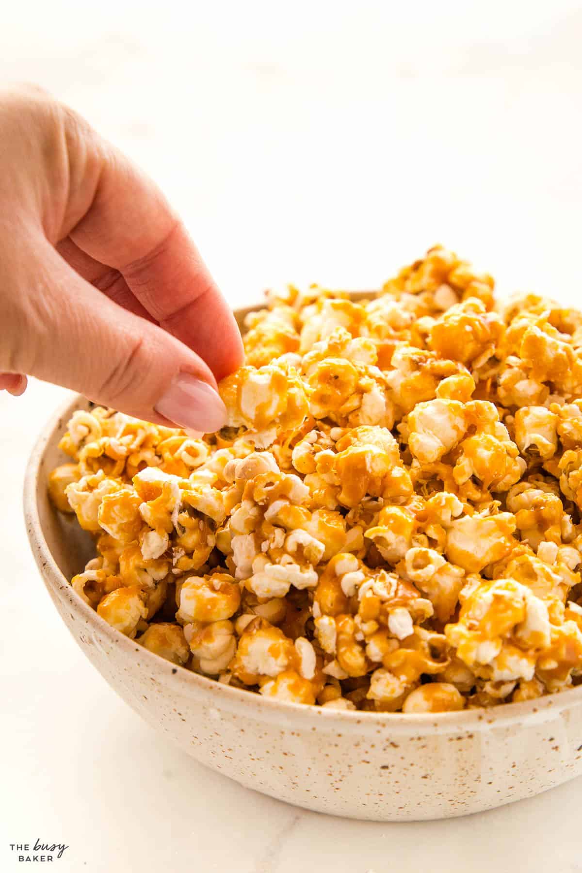 hand reaching for a piece of caramel popcorn from a ceramic bowls