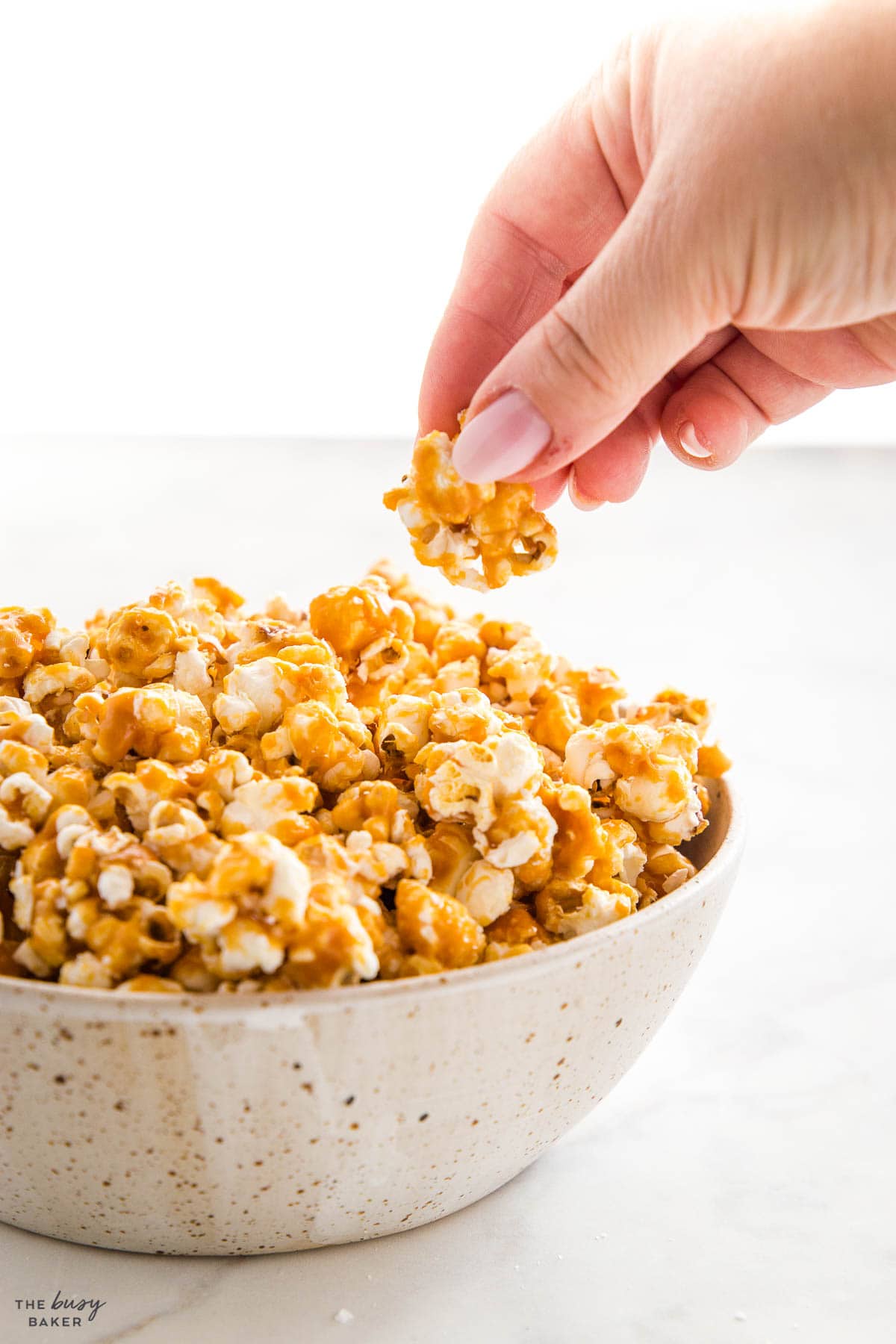 hand reaching for a piece of caramel popcorn from a bowl