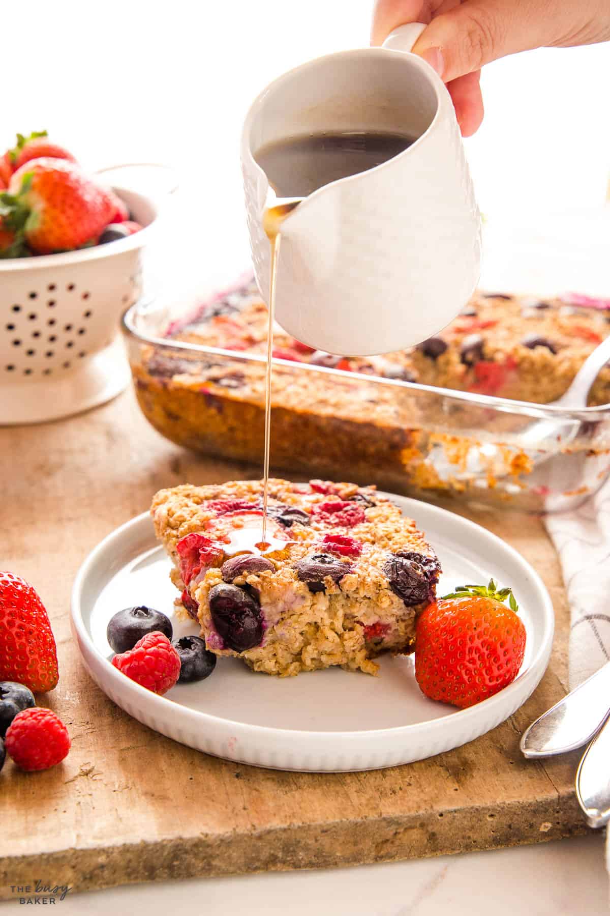 hand pouring maple syrup on baked oatmeal with berries