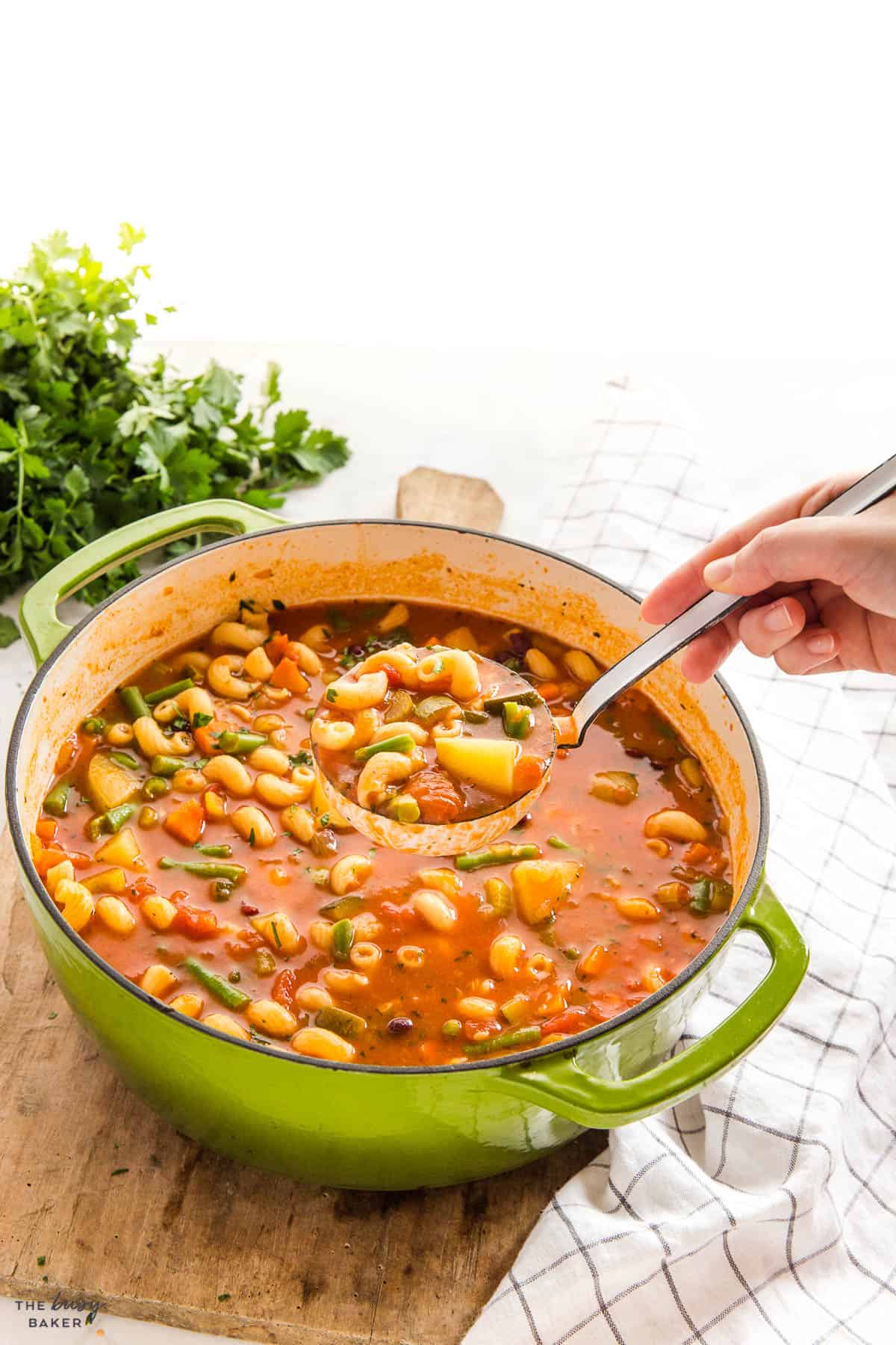 hand serving minestrone soup from a green pot