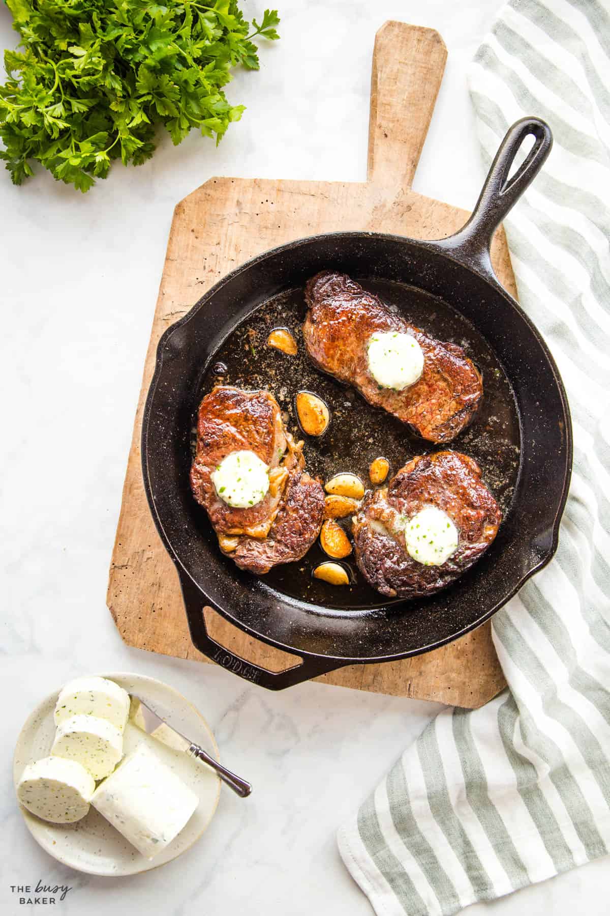 cast iron skillet with 3 pieces of steak and garlic butter